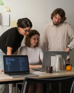 Three people stood around a laptop all looking at the screen