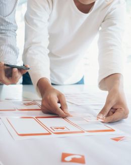 Two people arranging items of a webpage on a paper wireframe